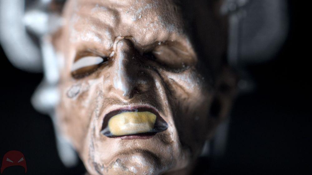 Close-up of a sculpted figure with a menacing expression, showing exaggerated features and a yellow-tinted tooth.